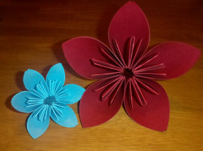 a small light blue paper flower next to a larger deep red paper flower